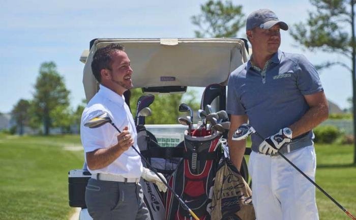 two golfers standing on course by cart with golf clubs