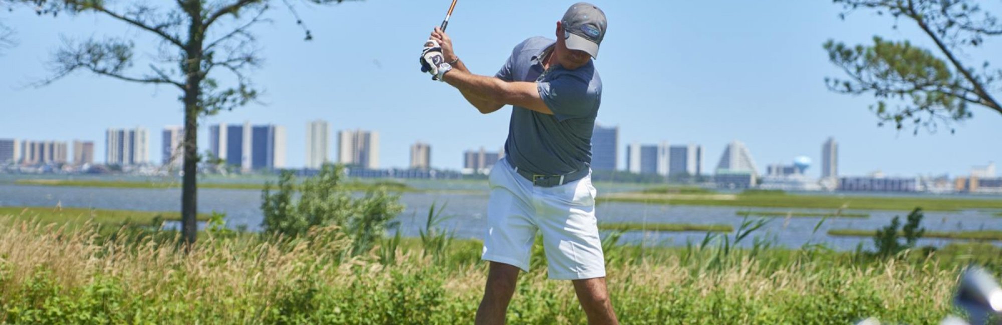 male golfer swinging golf club with ocean city md skyline behind him