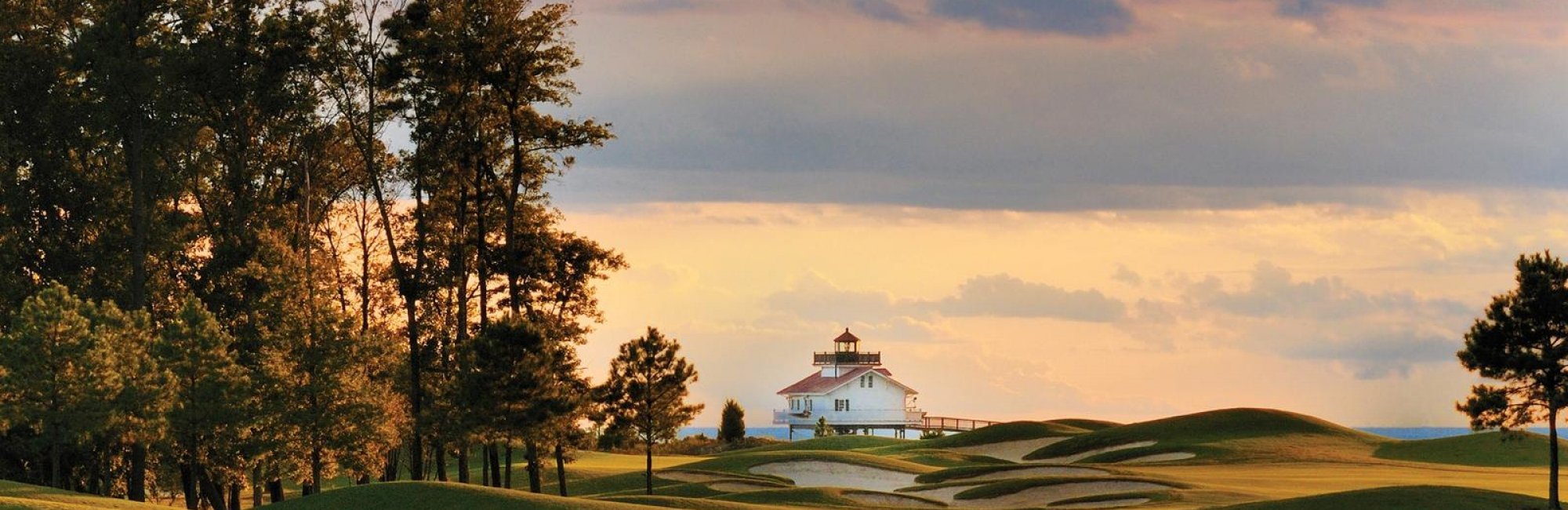 golf course with lighthouse and trees at sunset